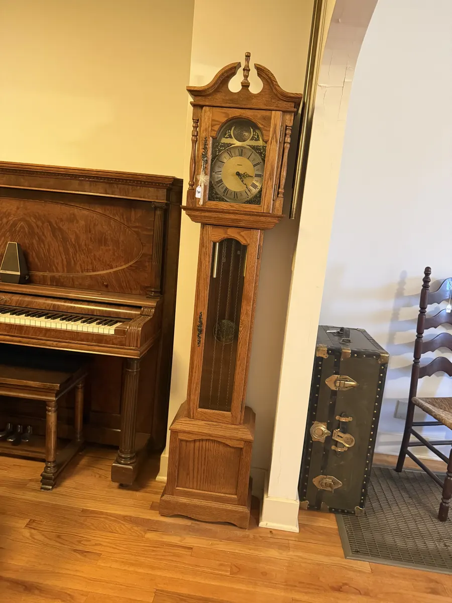 An upright piano and a tall grandfather clock in an estate-sale home.